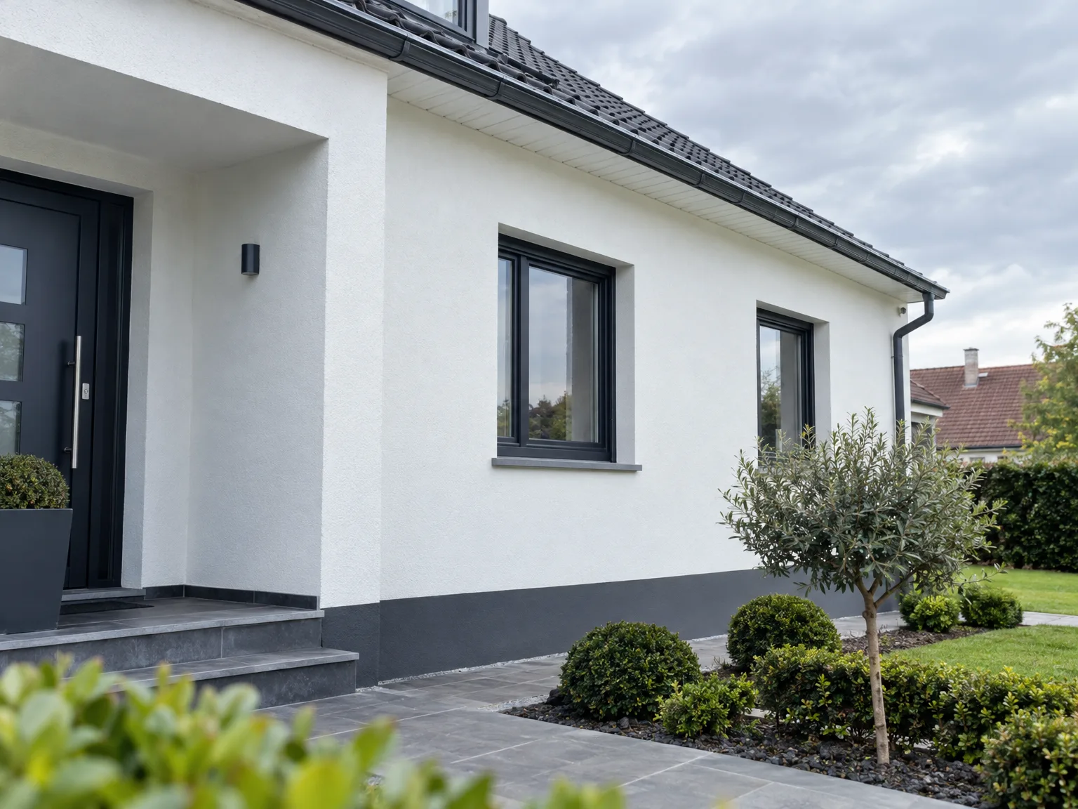 Maison avec ravalement de façade blanche, fenêtres noires, toit en ardoise et jardin paysager